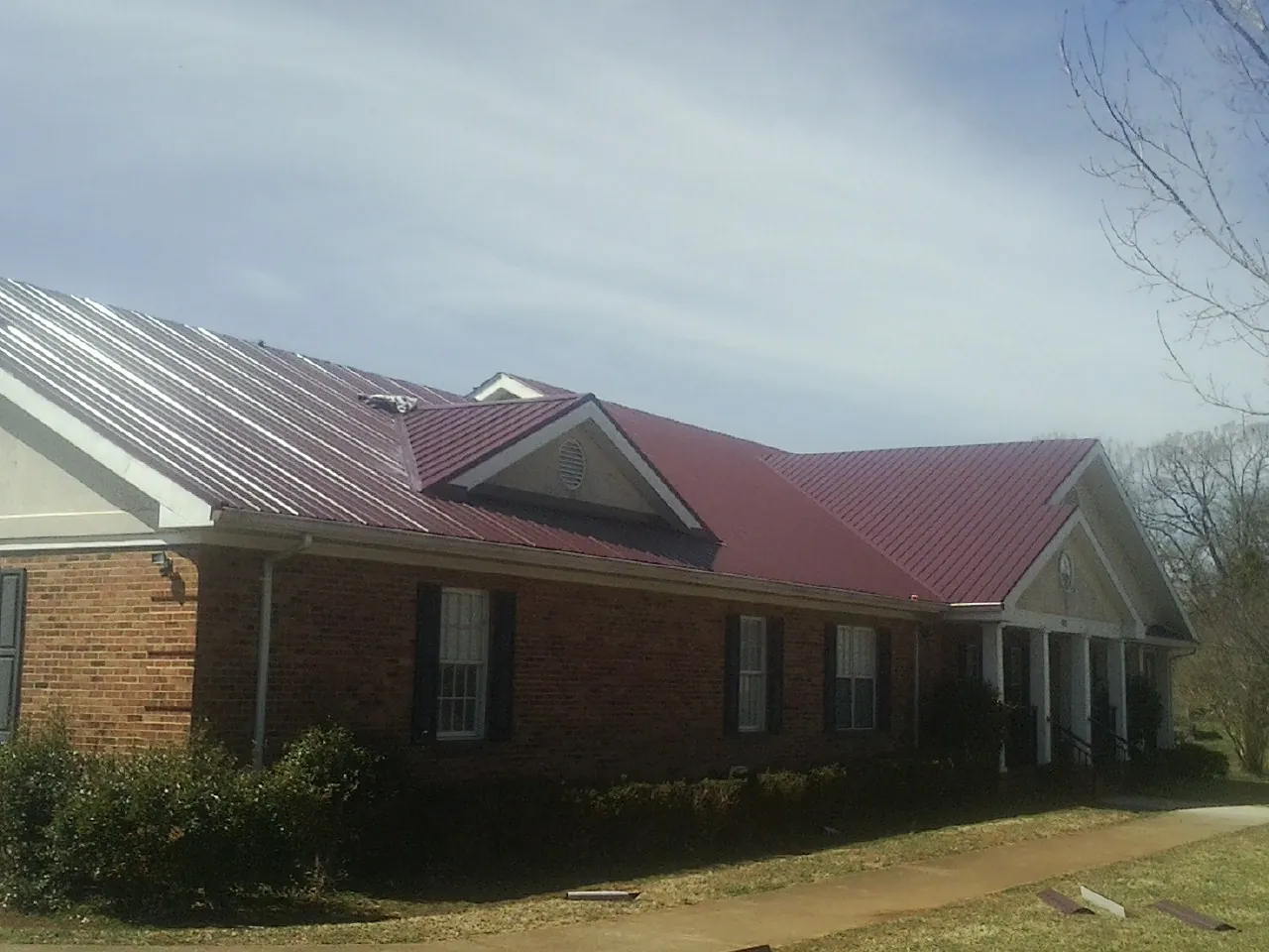 Red metal roof with gabled entries on a long brick building, from a Hail Damage Roof Repair job in Hopwood