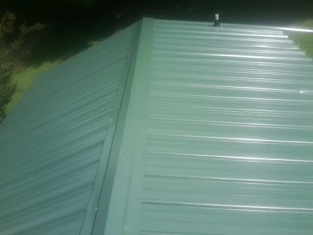 New green metal panels meeting at the ridge of a roof — Flat Roof Repair work by our crew in Hopwood
