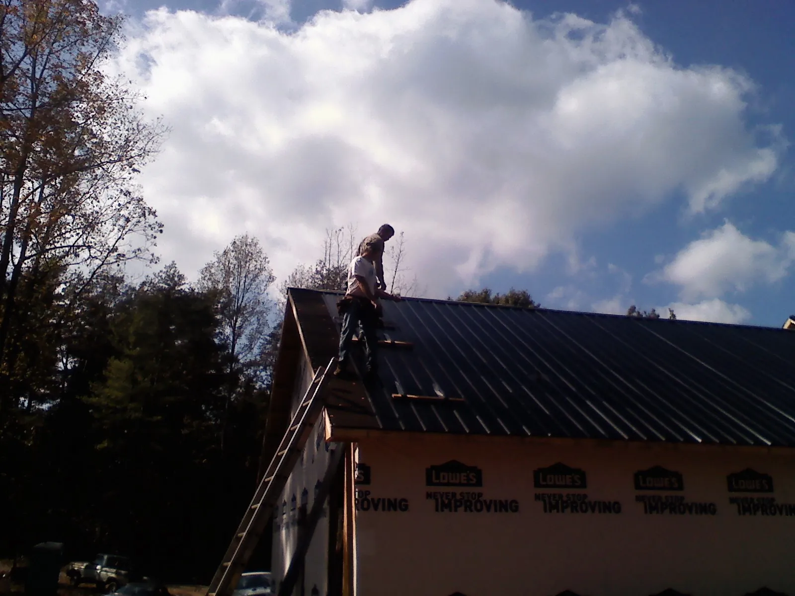 Roofer fastening dark metal panels high against a cloudy sky, from a Roof Inspection job in Hopwood