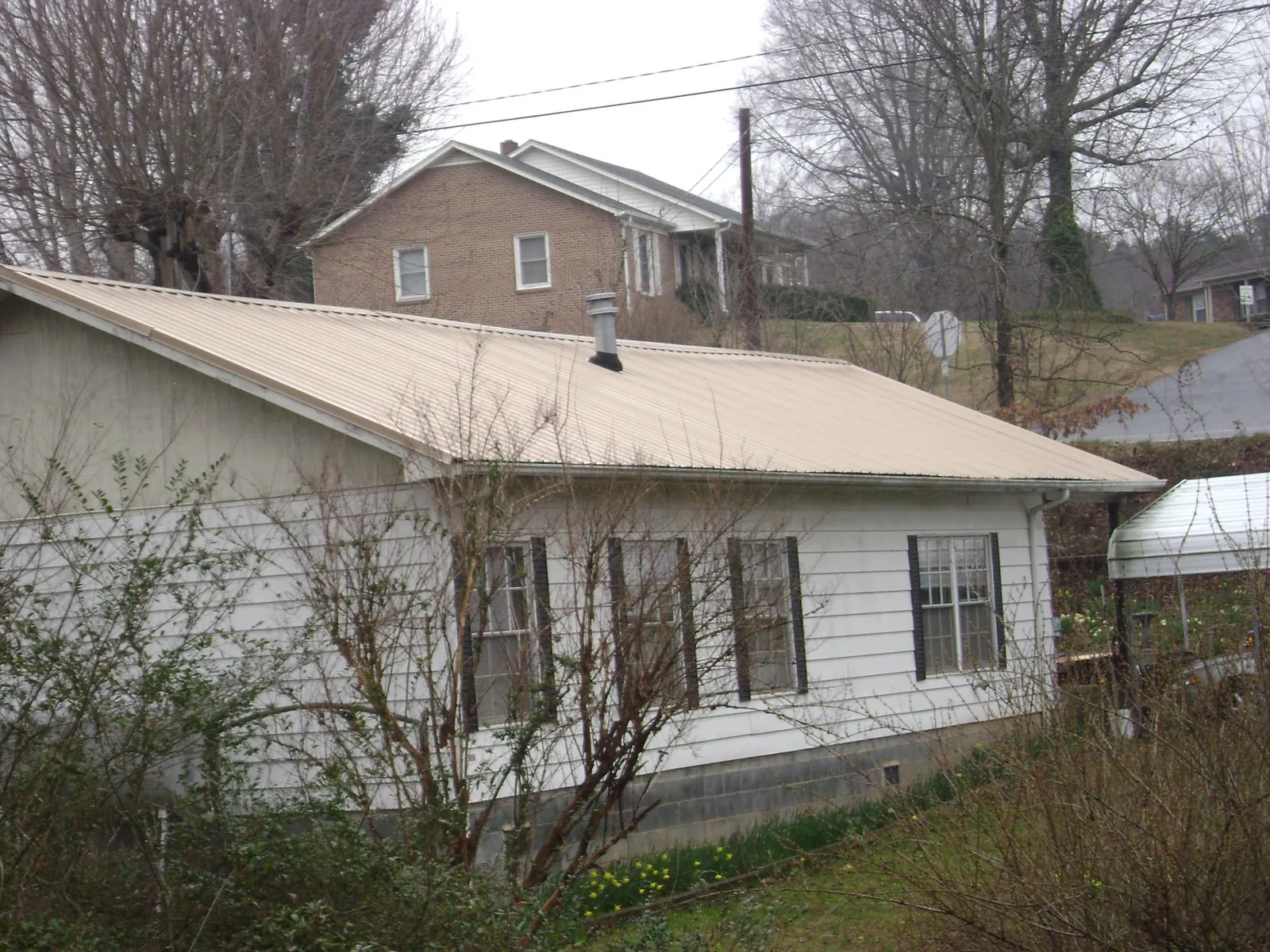 Tan metal roof on a white sided house set into a hillside — Commercial Roofing by Roofing Brothers in Hopwood