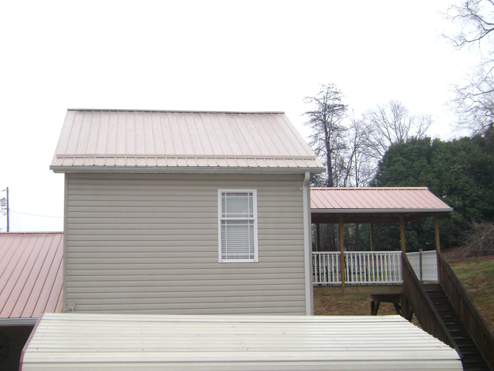 Tan metal roofs on a two story addition and attached porch, from a Roof Replacement job in Hopwood